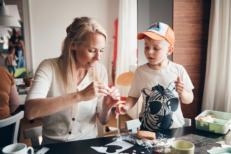 En frivillig i en familiecafé og en dreng sidder ved et bord og laver en kreativ aktivitet med papir